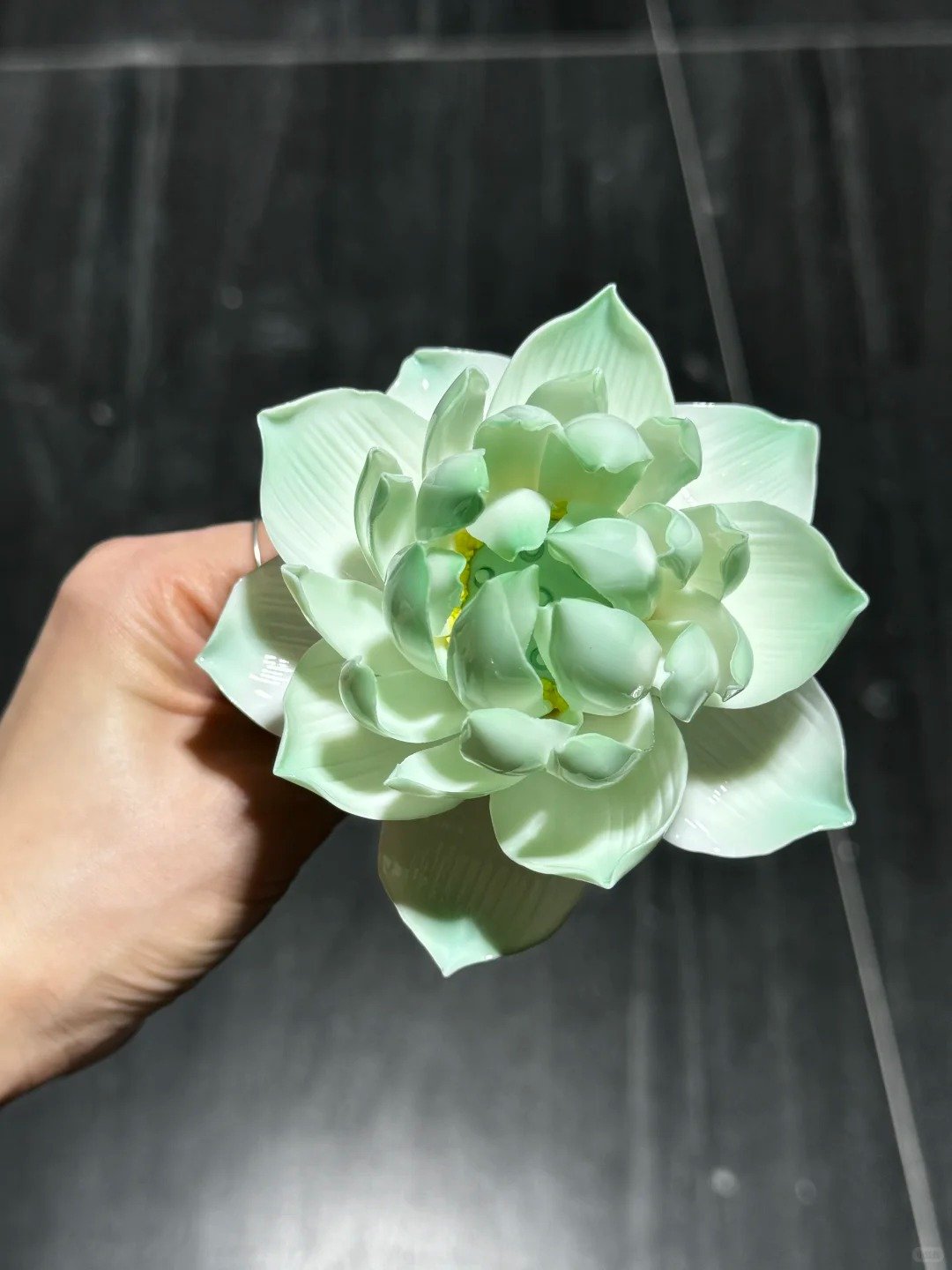 Hand holding a green lotus ceramic flower bouquet against a dark tiled background