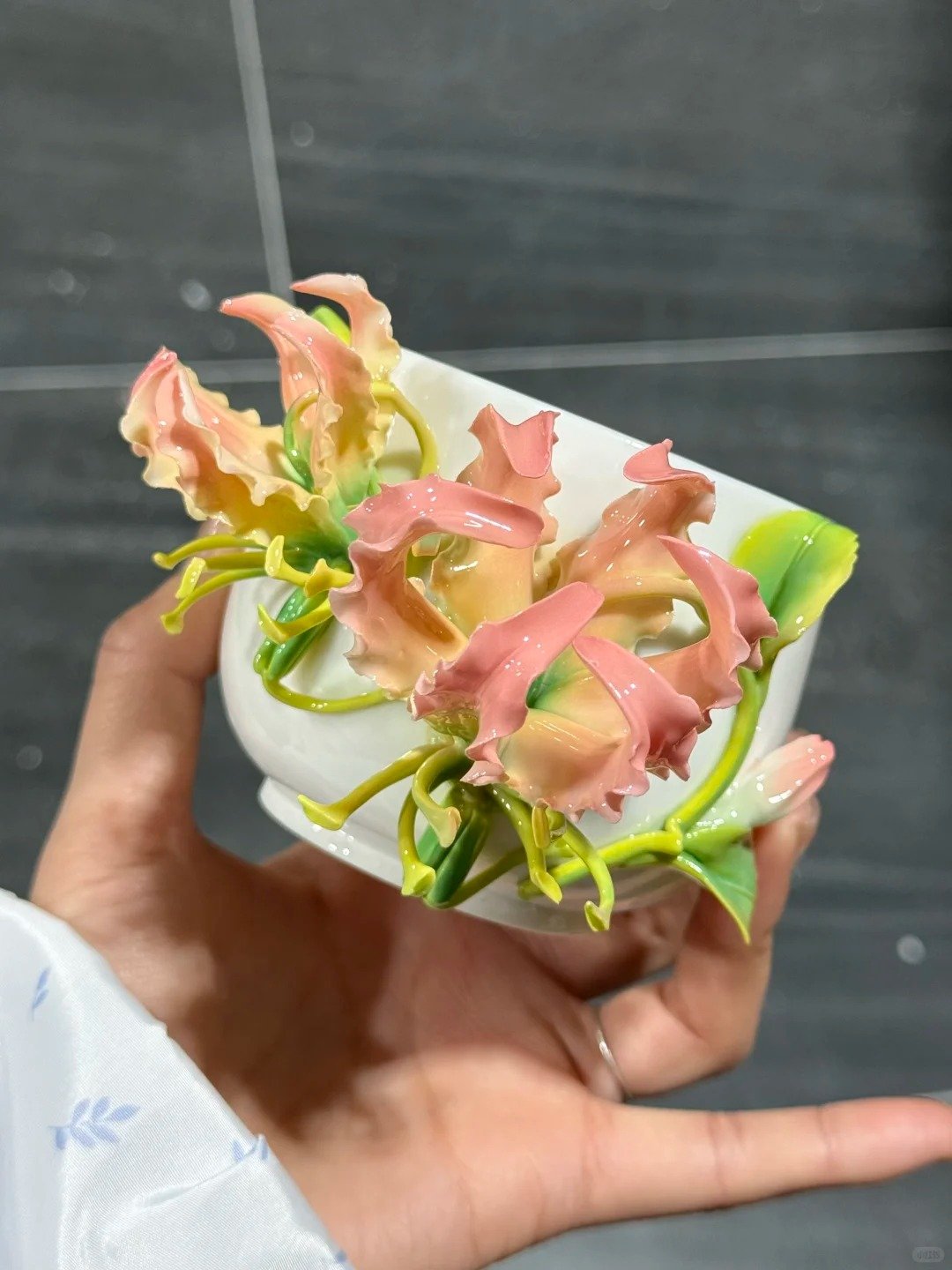 Hand holding a white cup decorated with pink lily ceramic flowers and green leaves
