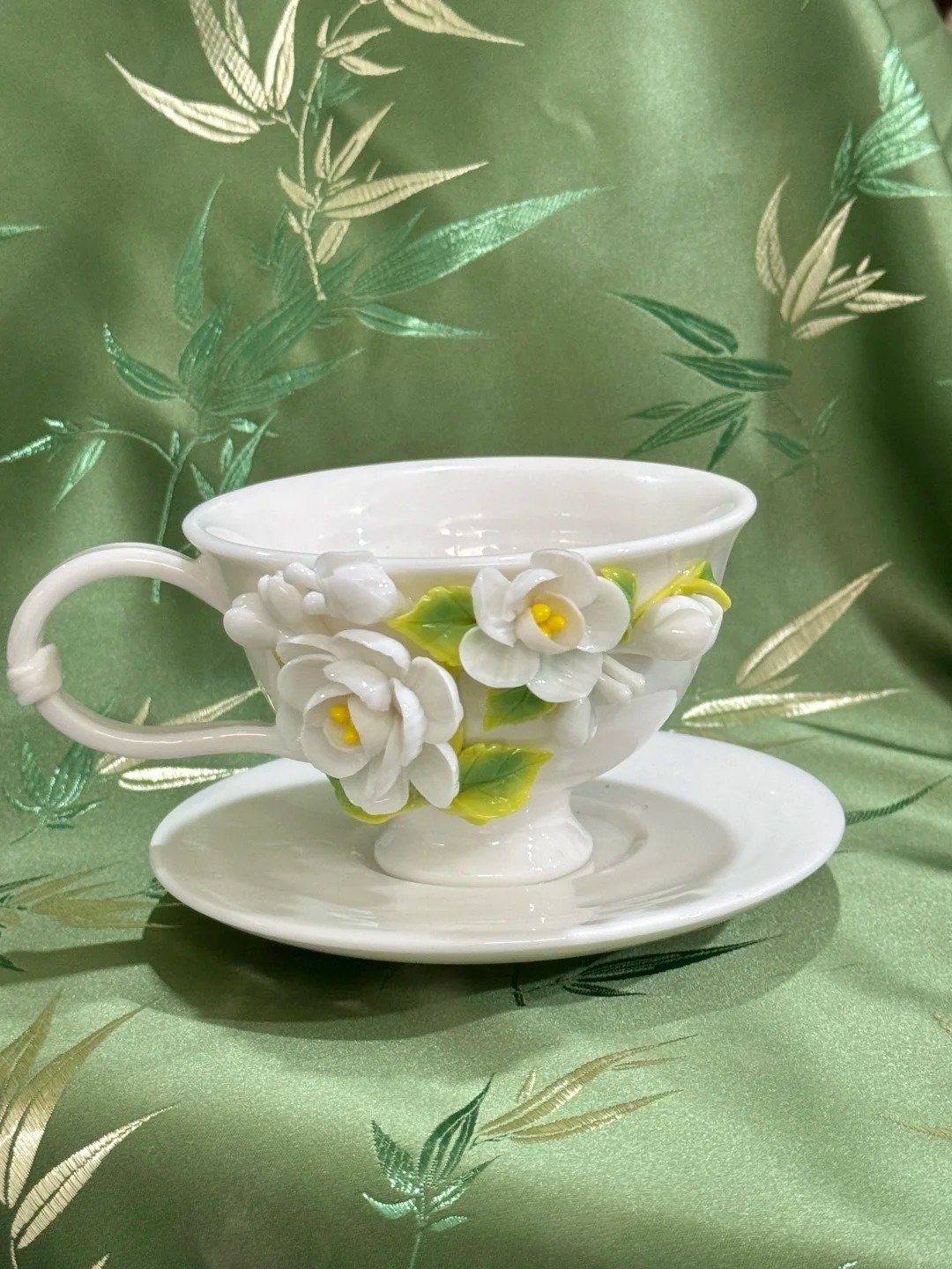 White jasmine ceramic flower cup displayed on a green floral fabric surface