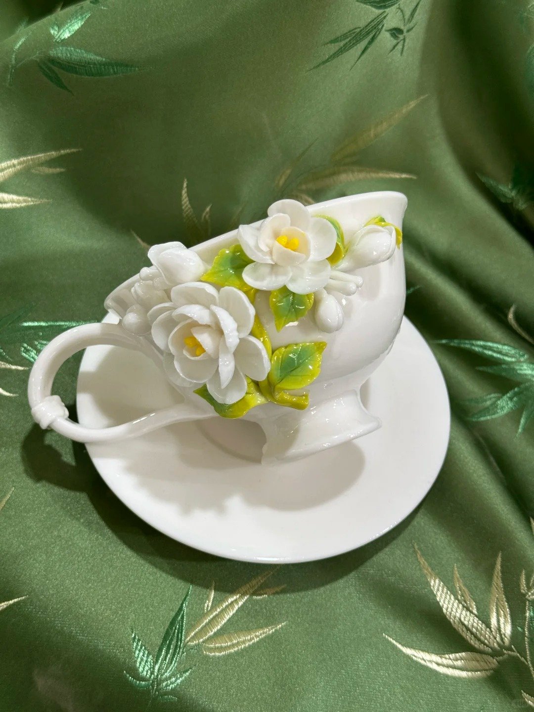 White ceramic coffee cup decorated with handmade jasmine ceramic flowers and green leaves