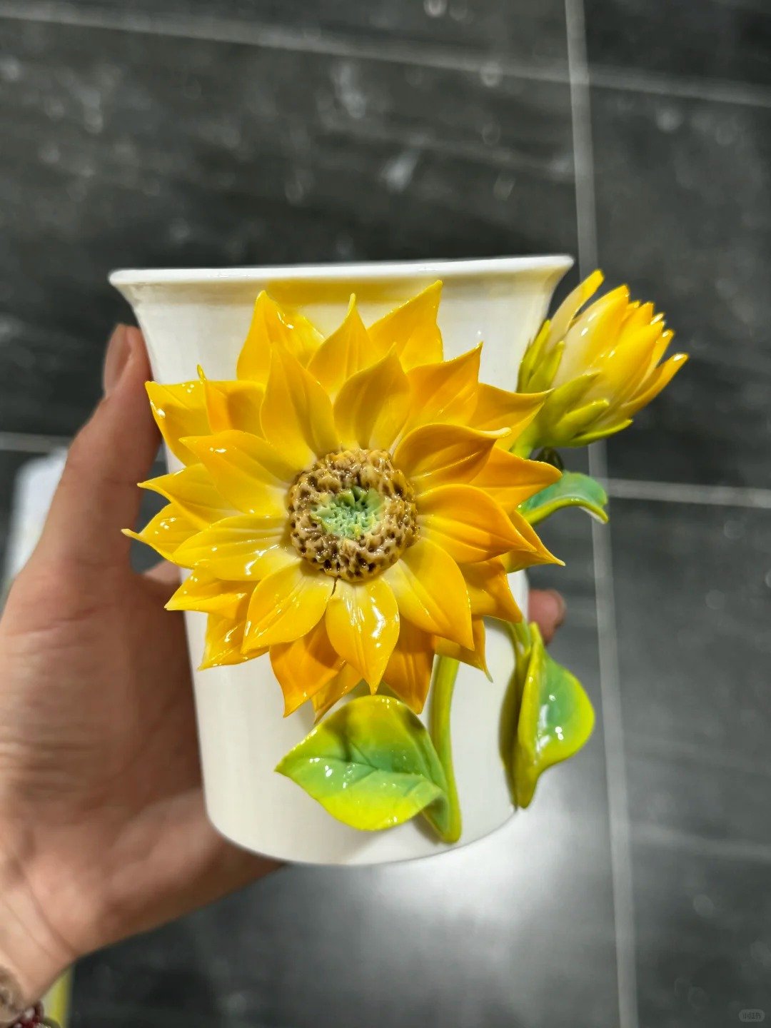 Hand holding a white ceramic cup decorated with yellow sunflower ceramic flowers