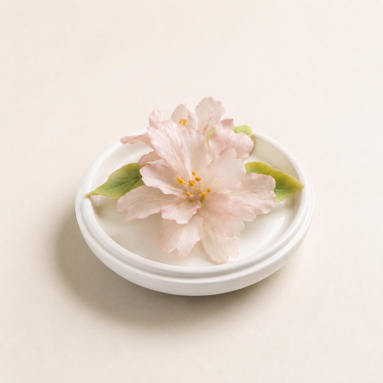 Pale pink begonia ceramic flower displayed in a simple white holder on a clean cream background